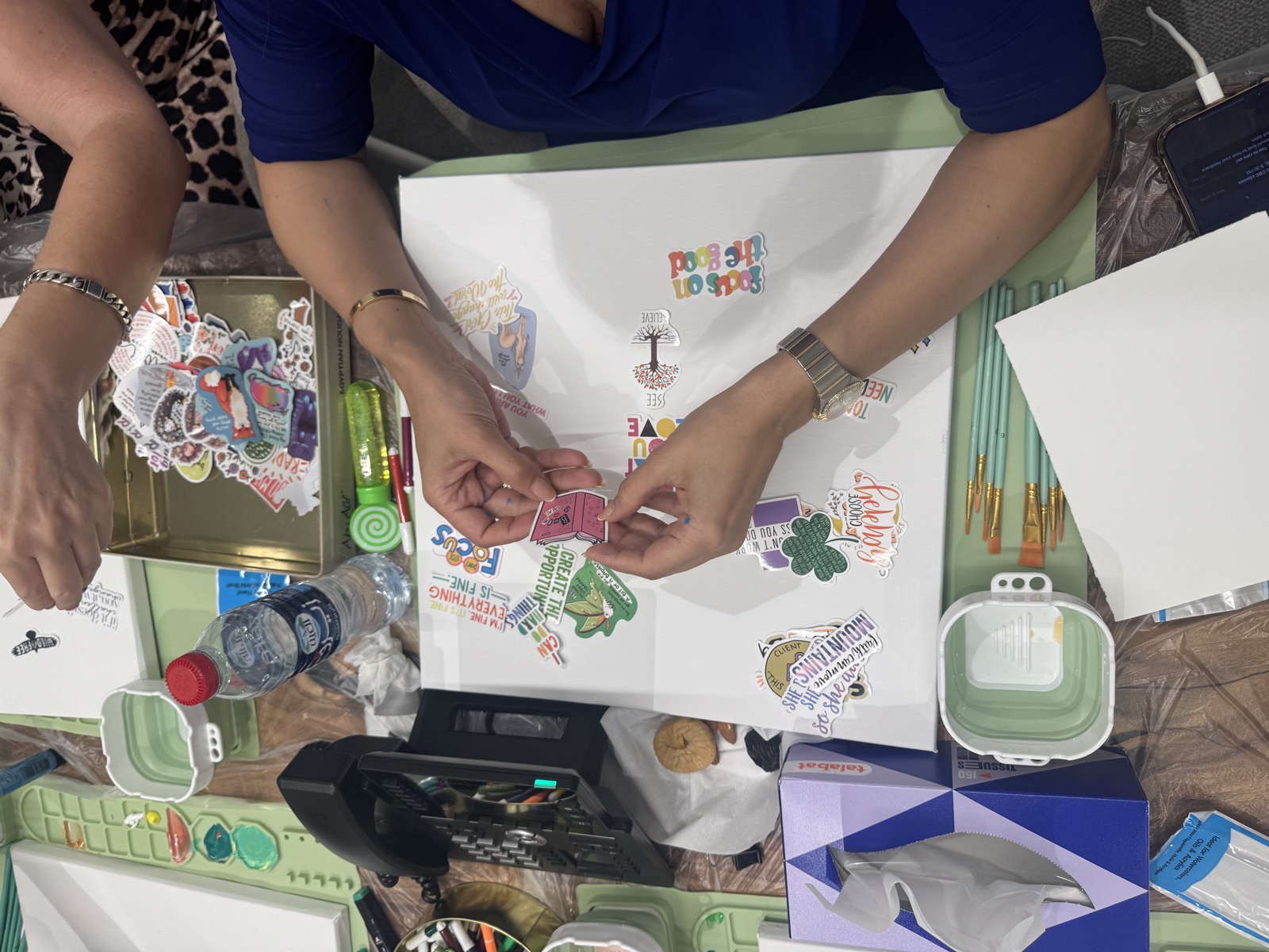 Hands placing cut paper onto a sheet, materials spread across the table